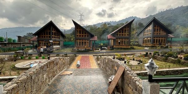 Four modern wooden houses with slanted roofs in a mountainous area under cloudy skies.