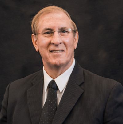 Portrait of a mature man in a suit and tie against a dark background.