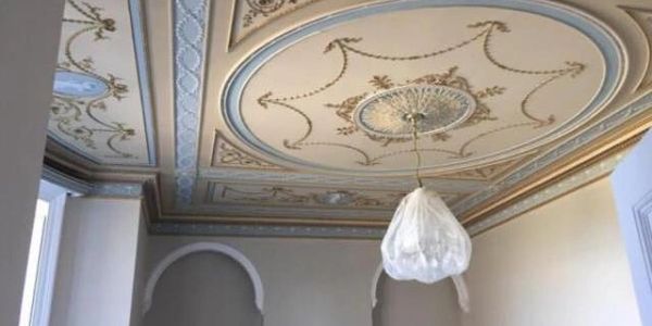 Ornate ceiling with detailed molding and a covered light fixture.