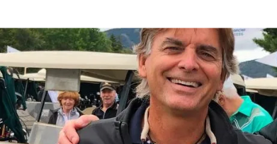 Smiling man outdoors near golf carts and people.