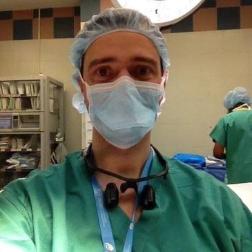 Medical professional in scrubs, mask, and cap in a hospital setting.