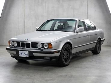 Silver BMW E34 sedan parked indoors with black wheels.