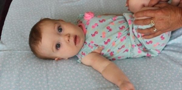 A baby lying on a blue blanket wearing a pink flamingo dress.