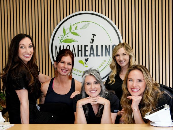 A group of five smiling women posing in front of a healing center sign.