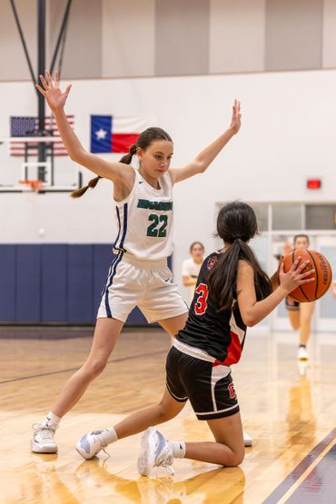 Girl basketball player in white defends against opponent with ball on the floor.