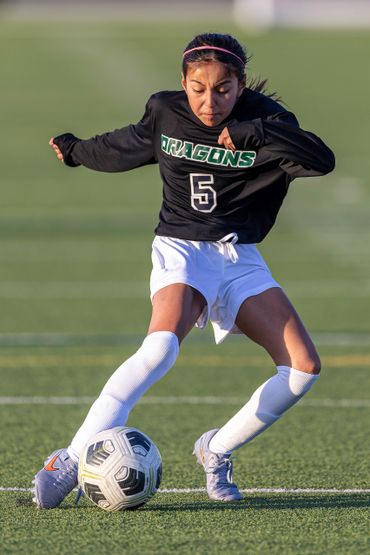 Young female soccer player in black jersey kicking a soccer ball on the field.