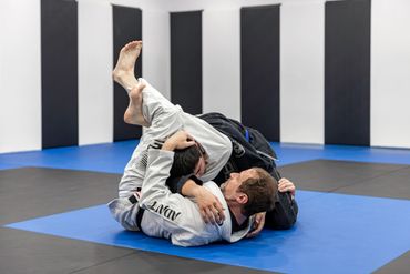 Two people practicing Brazilian Jiu-Jitsu on mats in a training room.