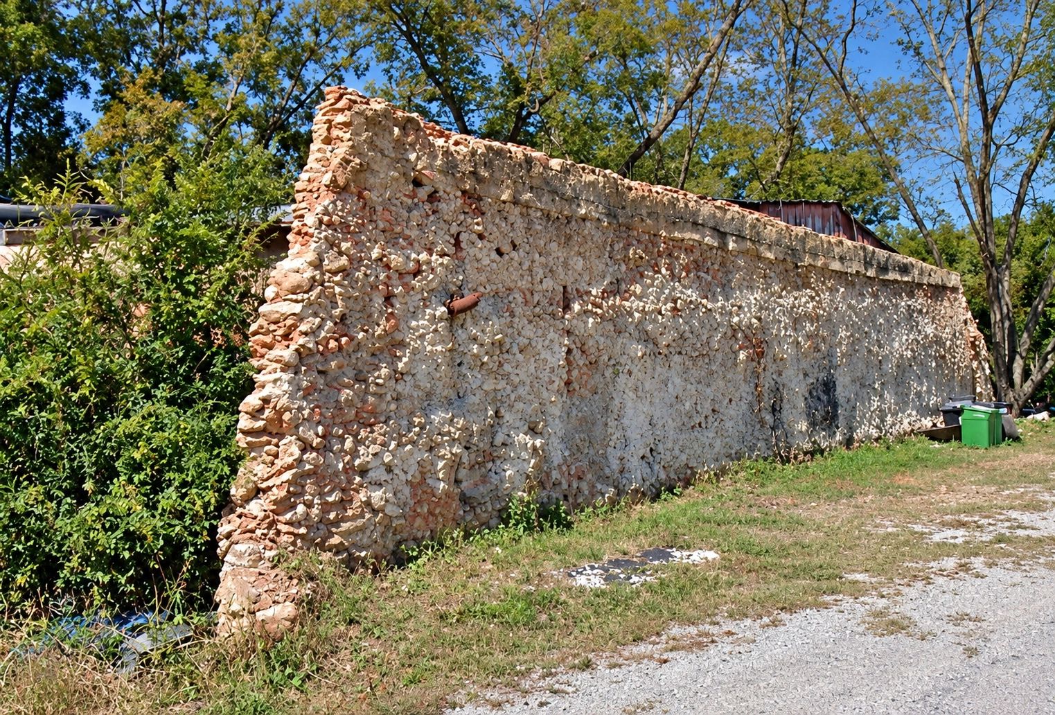 Old stone wall near trees and grass under blue sky.