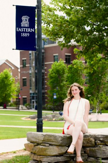 A woman in white sitting on a stone wall at Eastern University campus.
