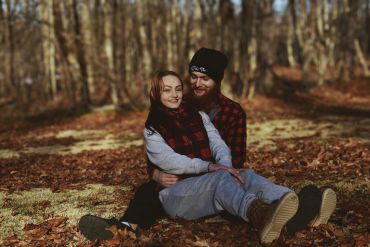 Couple sitting together in a forest during autumn, smiling warmly.