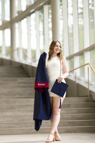 Young woman holding graduation gown and cap, smiling on stairs.