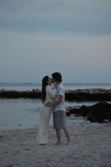 Couple sharing a tender kiss on a serene beach at dusk.