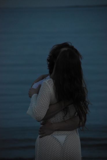 Couple embracing intimately by a calm body of water at dusk.