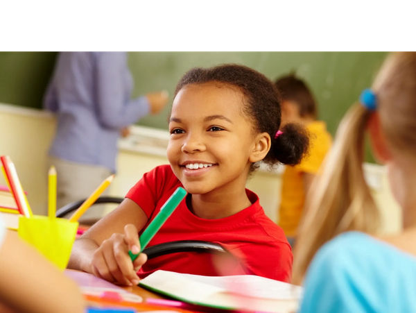 A smiling girl in a classroom holding a green marker.