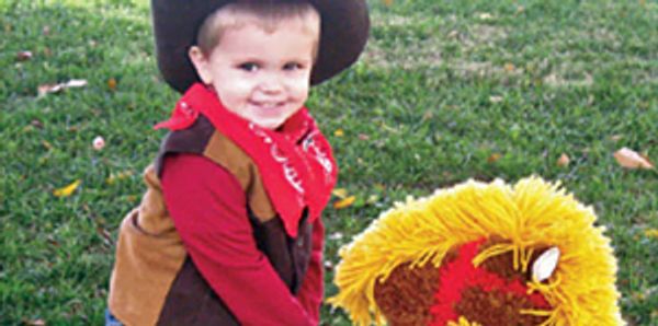 A young boy dressed as a cowboy with a toy horse.