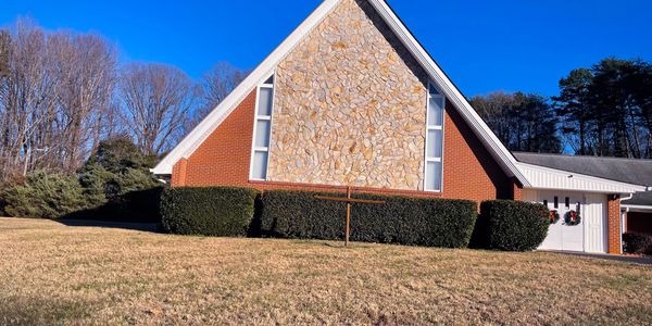 A brick church with a stone facade and Christmas wreaths on the doors under a clear blue sky.