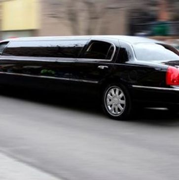 A black limousine driving fast on a city street with blurred background.