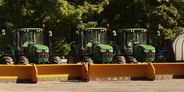 Three green tractors with yellow snow plow attachments parked side by side.