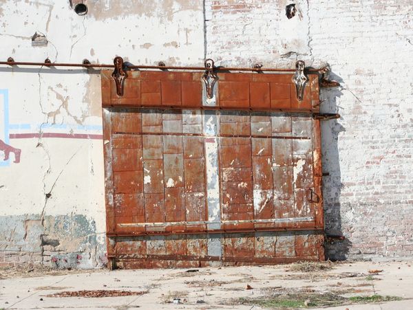 Rusty metal sliding door on a weathered brick wall.