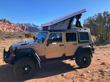 Yellow Jeep Rubicon with a pop-up camper top parked beside a dirt road in the desert.