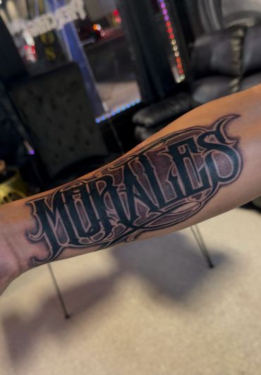 Forearm tattoo of the word 'MURALES'.
