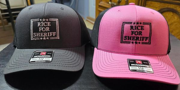 Two trucker hats with 'Rice for Sheriff' embroidered on the front.