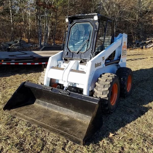 A Bobcat 863 skid-steer loader with a front bucket on grassy ground.