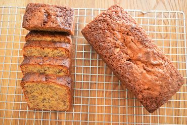 Slices of banana bread laid out on a cooling rack next to another full loaf of banana bread.