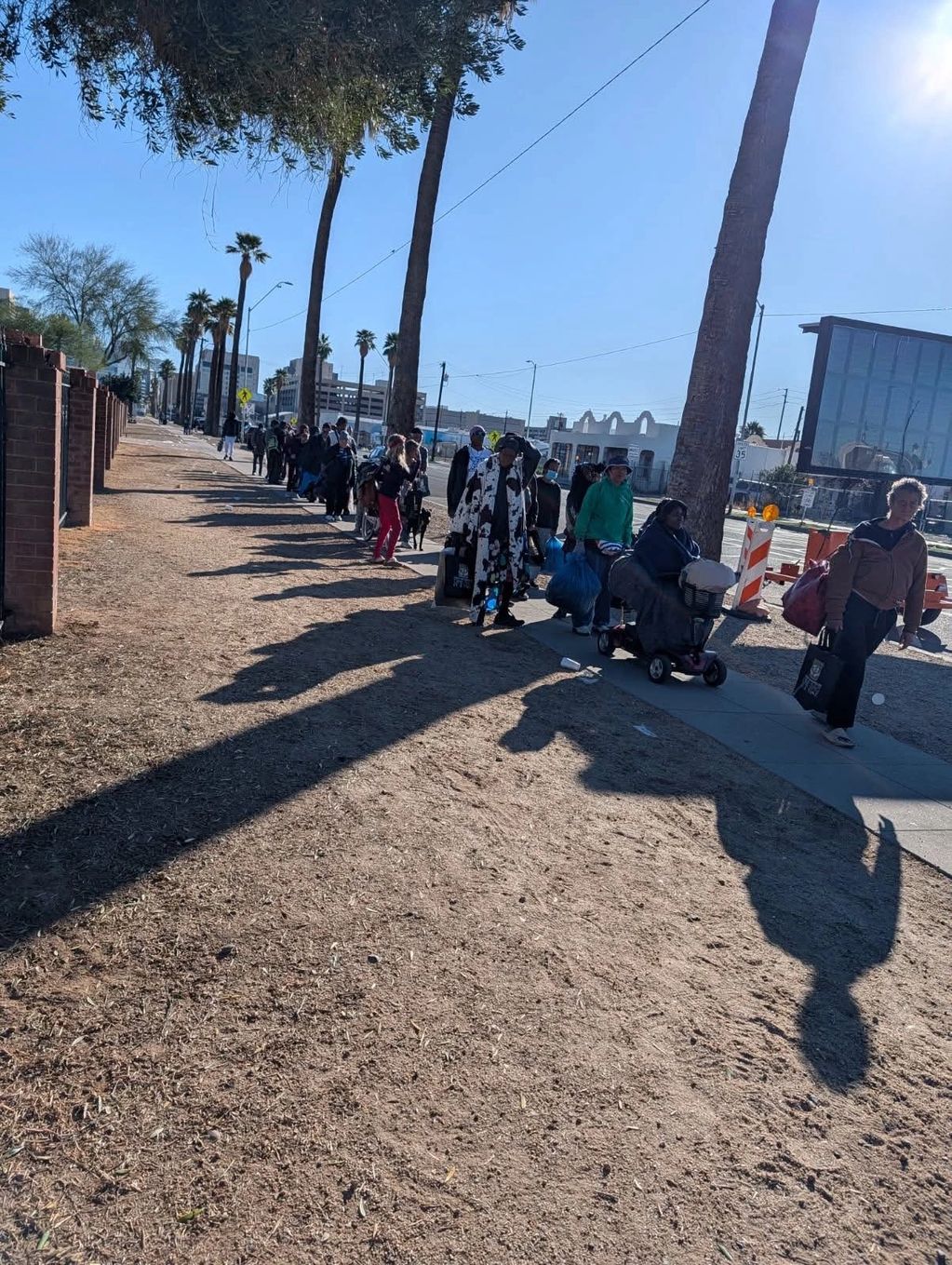 People lined up along a sidewalk on a sunny day.