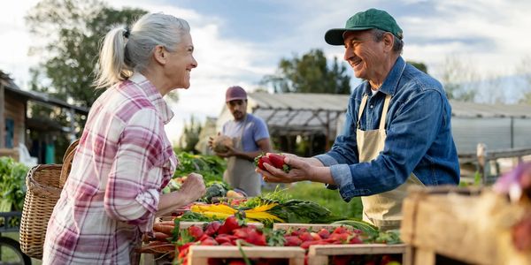Elderly woman buying strawberries from a cheerful vendor at an outdoor market.