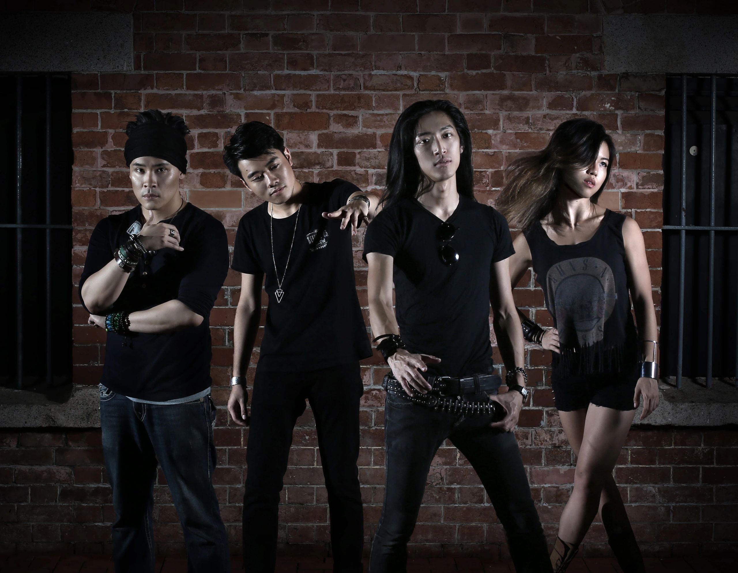 Four young adults in edgy black outfits posing against a brick wall.
