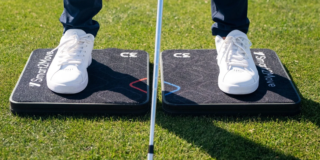 Person standing on two black balance pads with white shoes on grass.