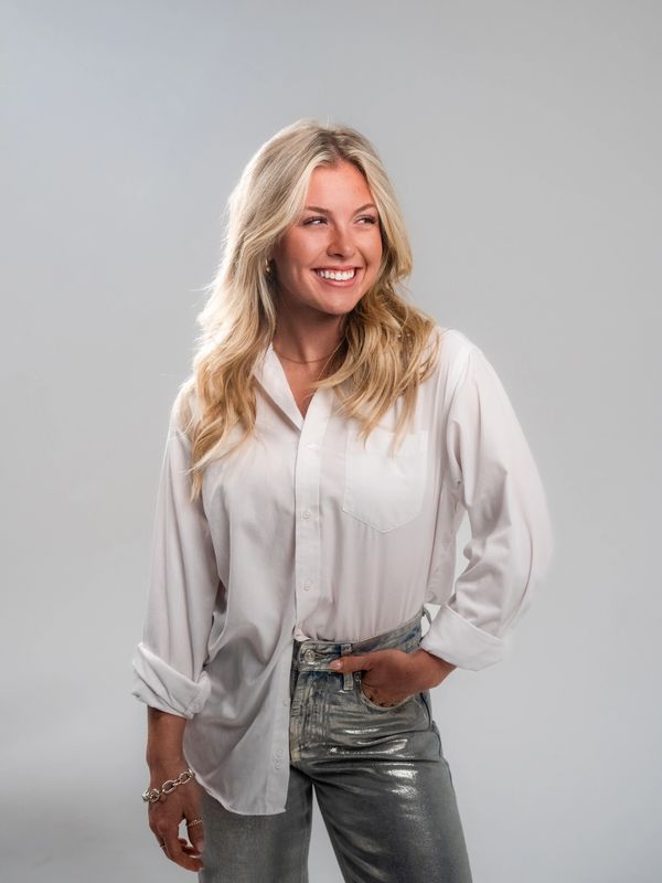 Smiling woman in a white shirt and shiny silver jeans posing confidently.