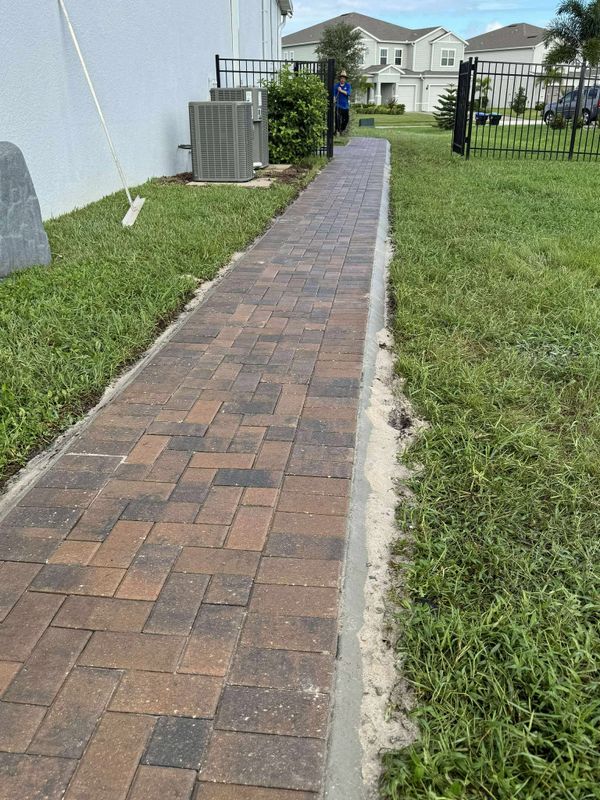 Newly paved brick pathway leading to a fenced backyard gate.