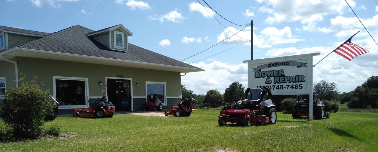 Image of front of building with business sign and rider mowers on the grounds.