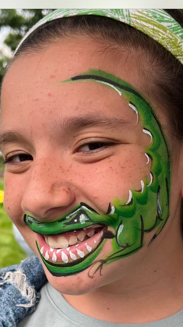 Girl with alligator face paint smiling outdoors.