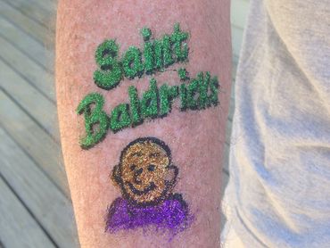 Arm tattoo of 'Saint Baldrica' with a cartoon face.