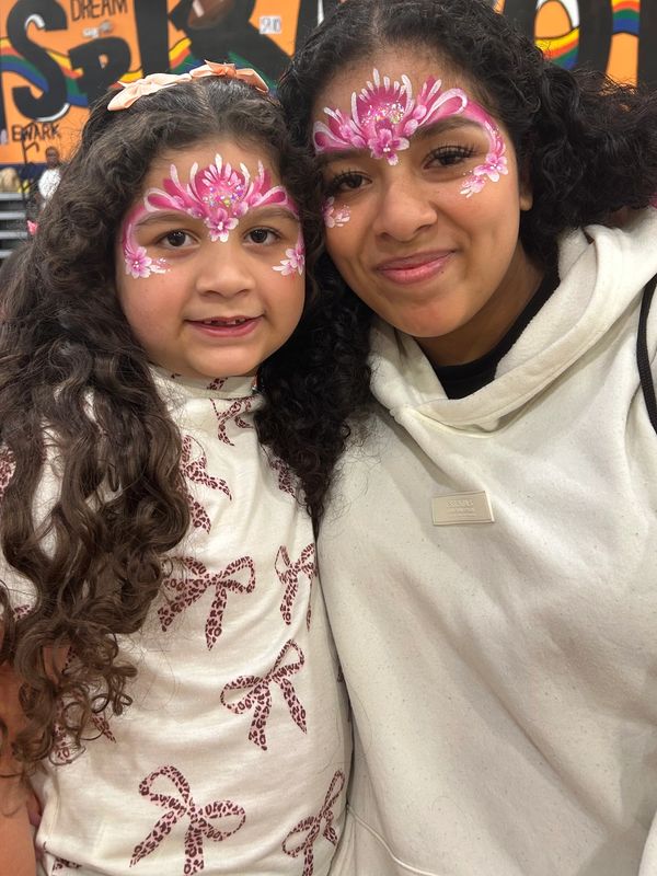 Two girls with pink face paint smiling.