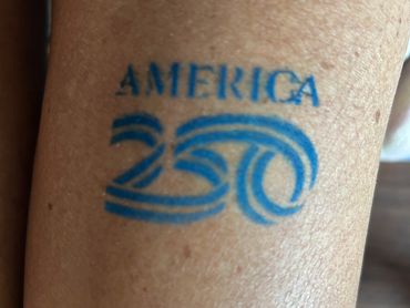 Tattoo reading "AMERICA 250" on skin.