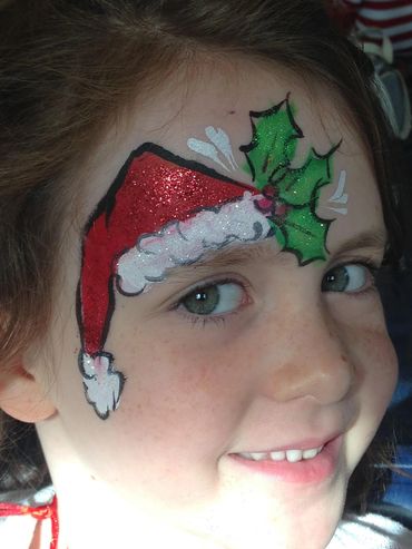 Child with festive face paint of a Santa hat and holly.