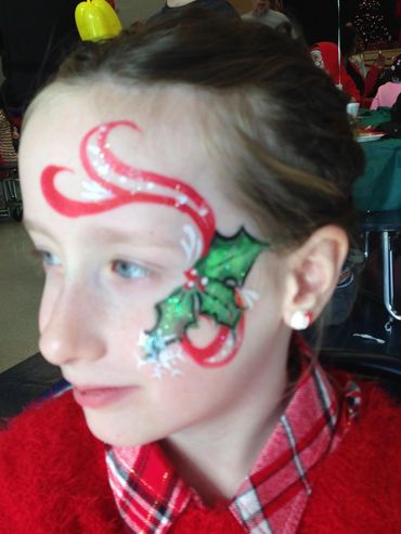 Child with festive face paint of holly and red swirls.