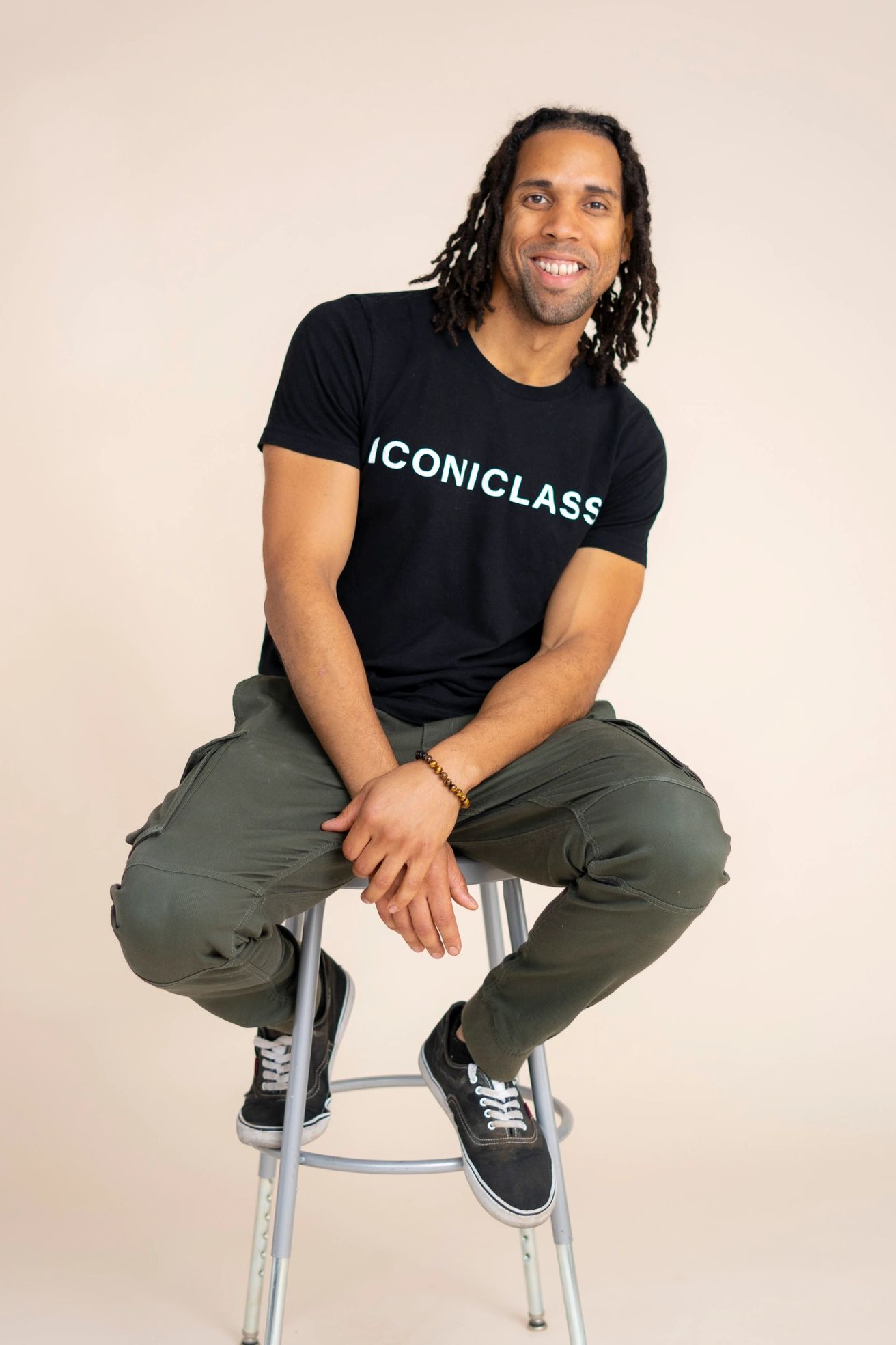 The founder smiling while seated on a stool wearing an "ICONICLASS" branded shirt.