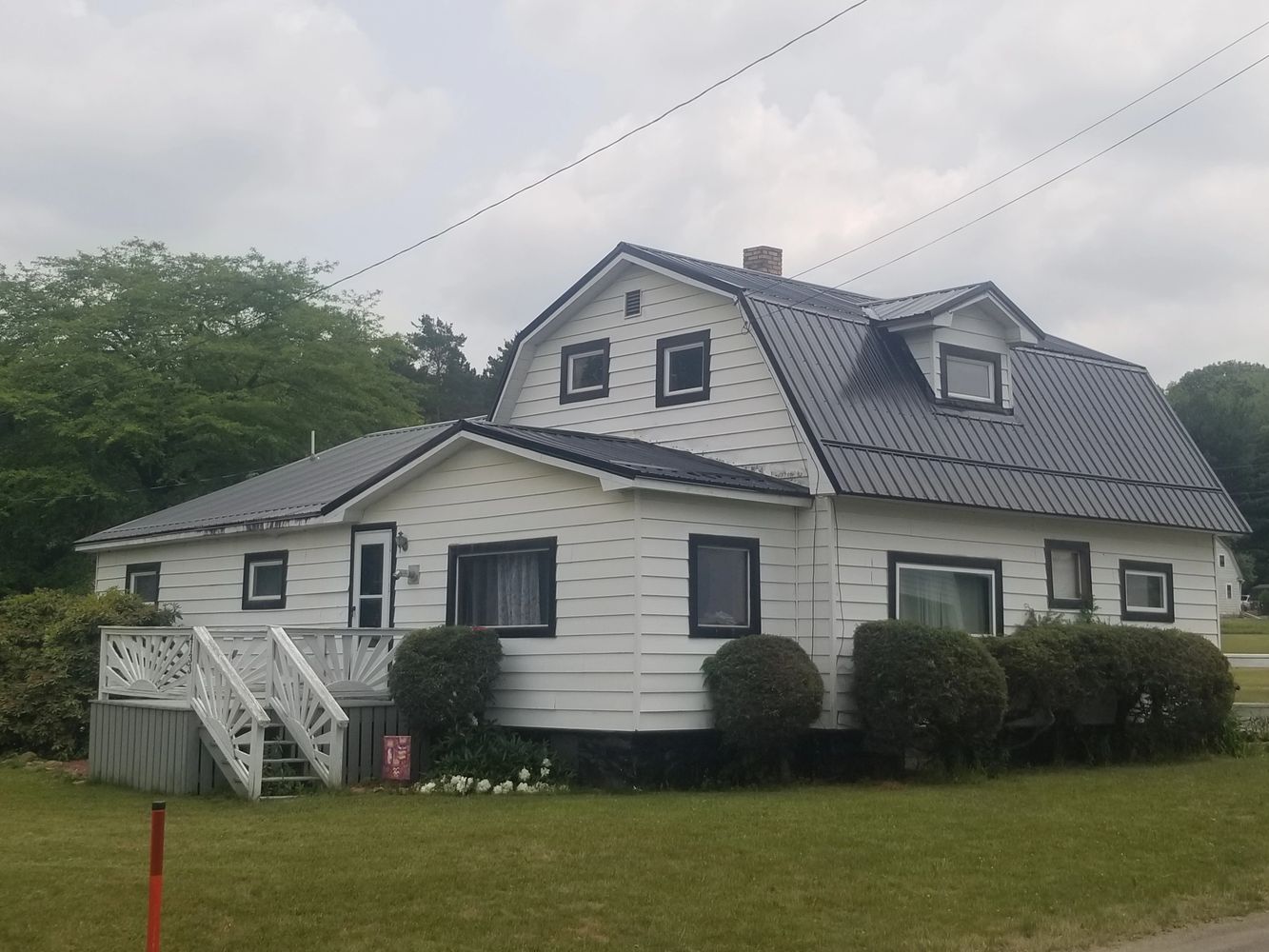 White house with black trim and metal roof surrounded by bushes.