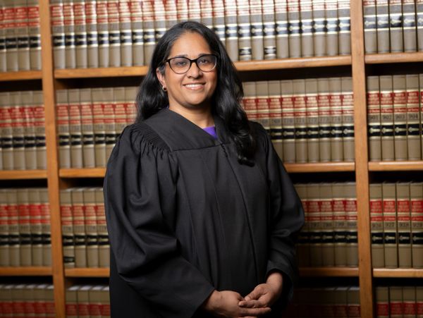 A woman in a judge's robe stands in front of law bookshelves.