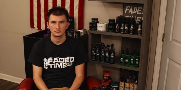 A man wearing a "Faded Times" t-shirt sits beside shelves of grooming products.