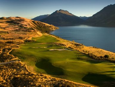 Scenic golf course beside a lake and mountains.
