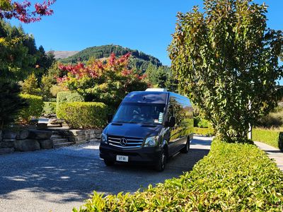Black Mercedes van on a scenic road with greenery and hills.