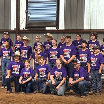 Group of smiling young people in matching purple shirts posing indoors.