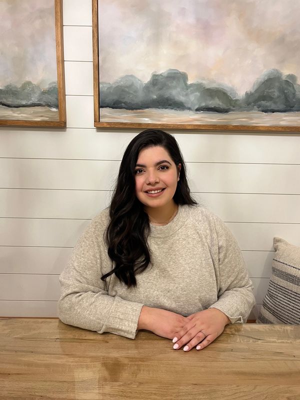Smiling woman with dark hair sitting at a wooden table in a cozy room.