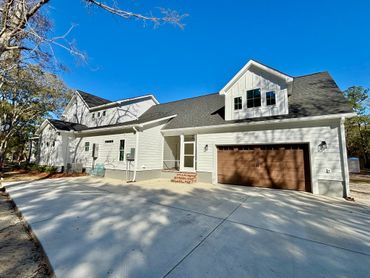 Modern white house with a spacious driveway and wooden garage door under clear blue sky.
